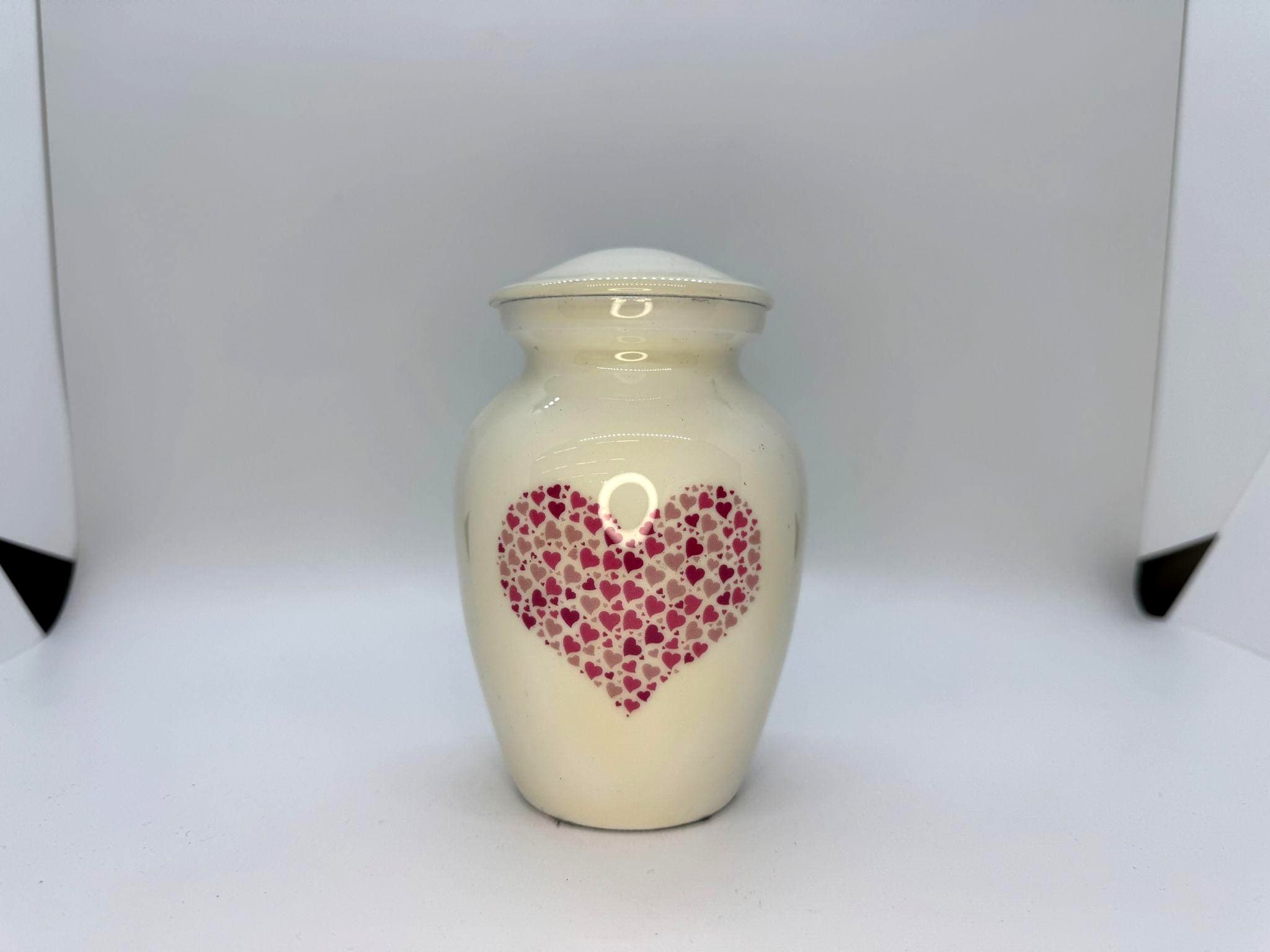 Cream-colored alloy urn with pink heart accents.
