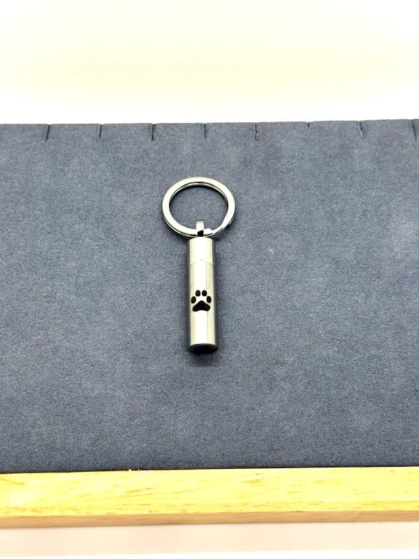 Silver cylinder keychain with black paw print accent.