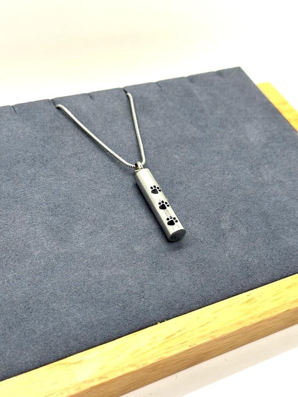 Silver cylinder necklace with black paw print accents.