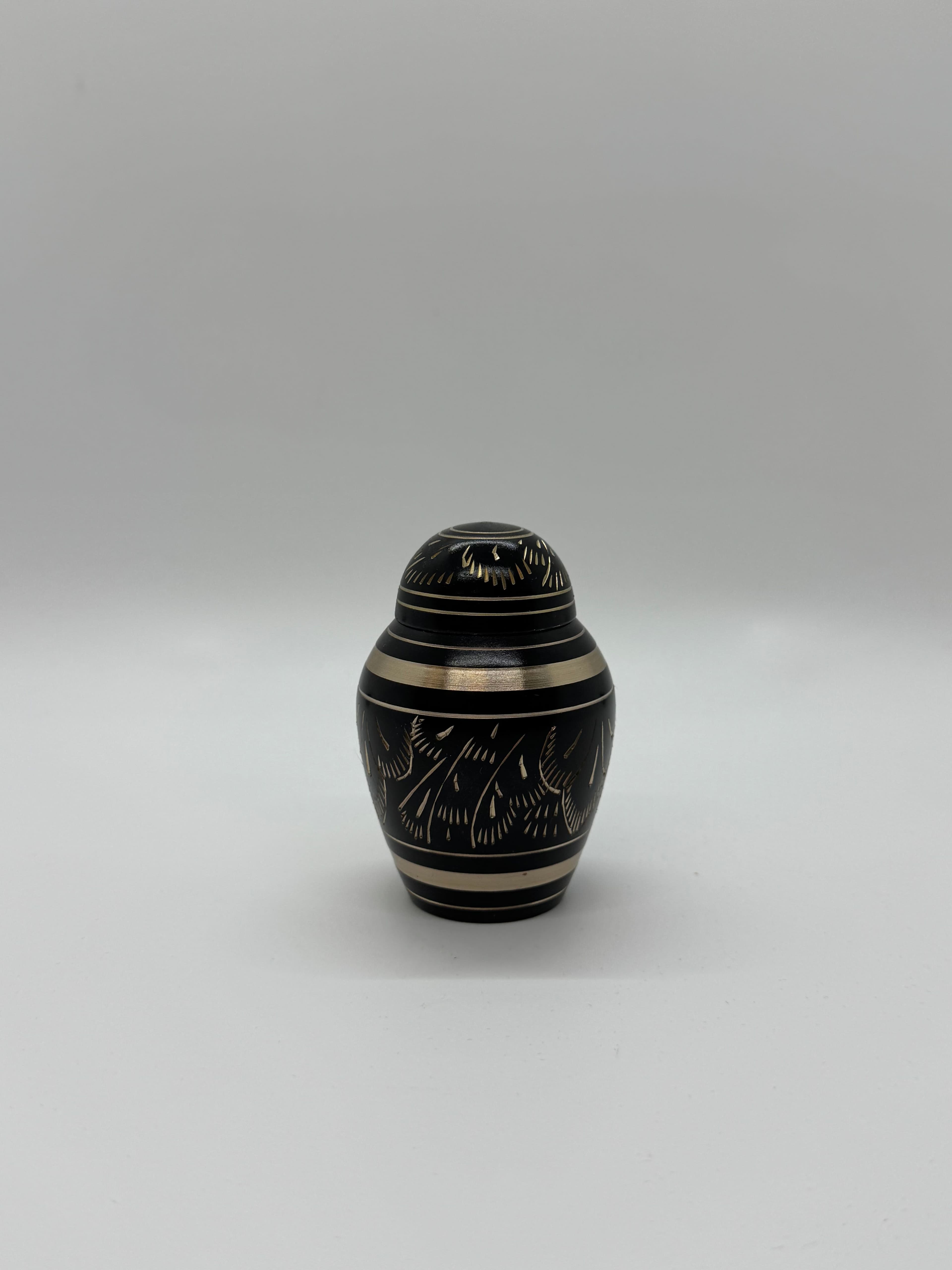 Black metal keepsake urn with gold color engraving embellishments featuring a domed top.