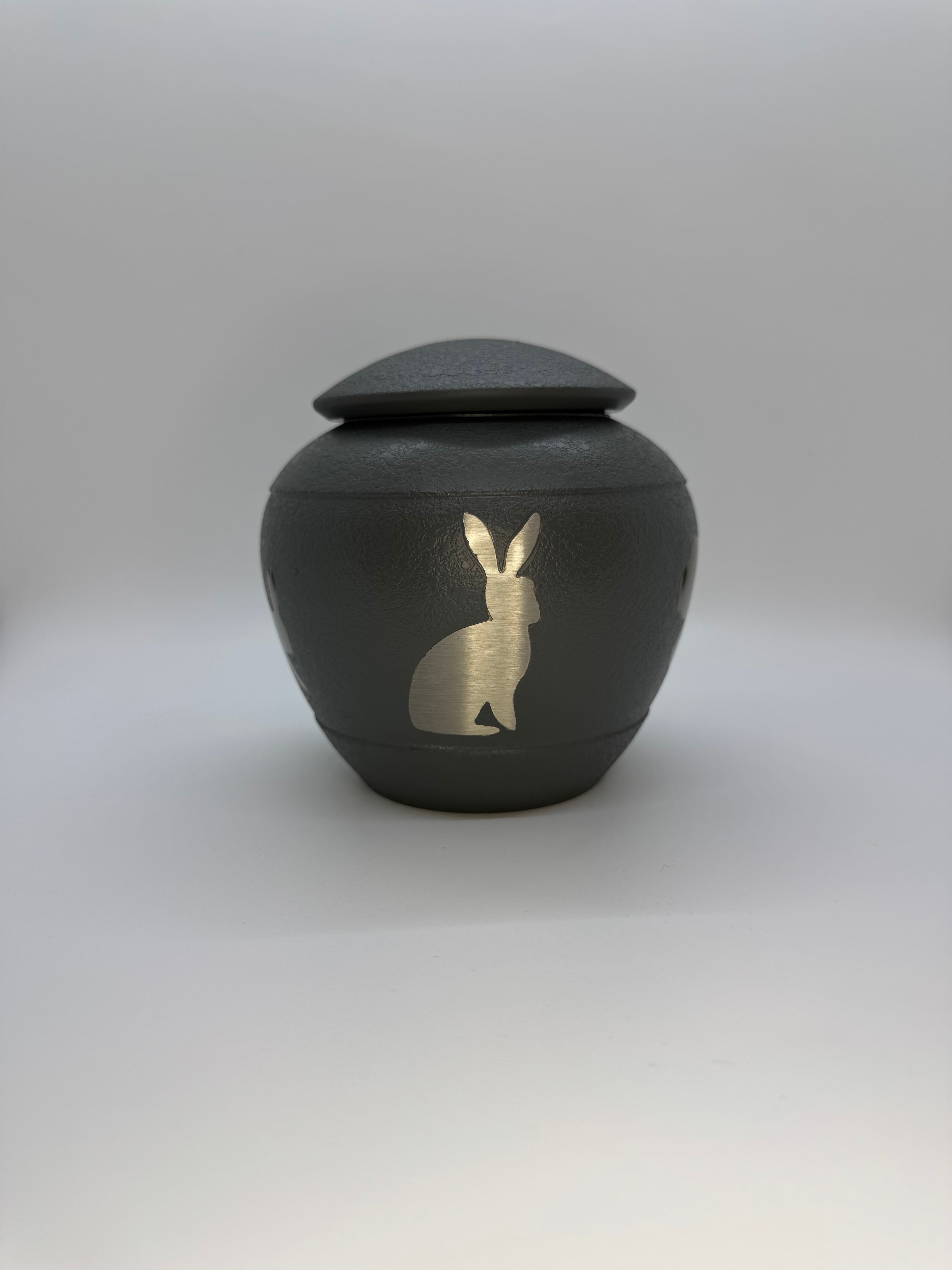 Cool grey metal urn featuring a bunny silhouette hopping around the urn.