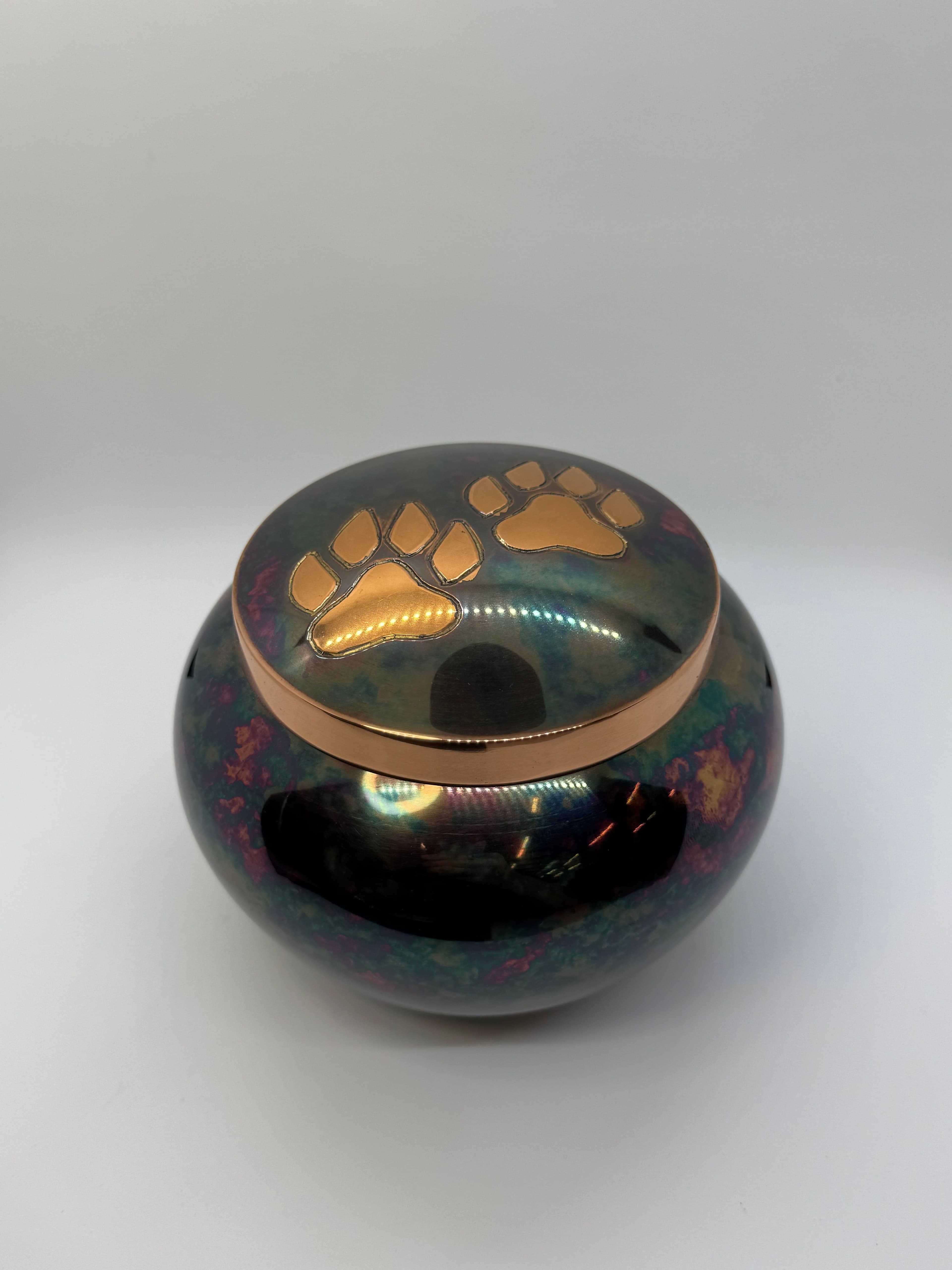 Metal urn featuring a rake finish and golden paws on top.
