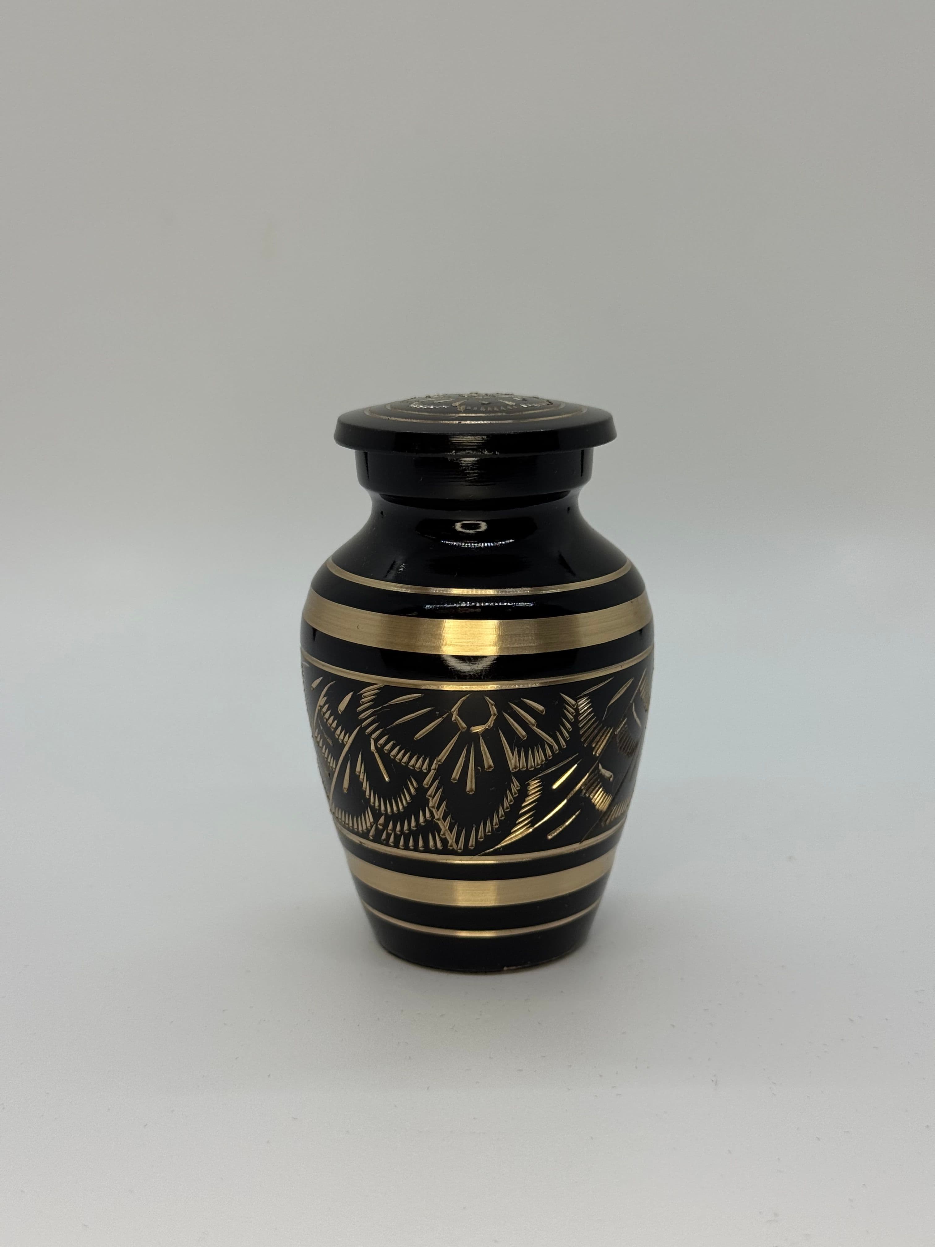 Black metal keepsake urn with gold color engraved embellishments featuring a flat top.