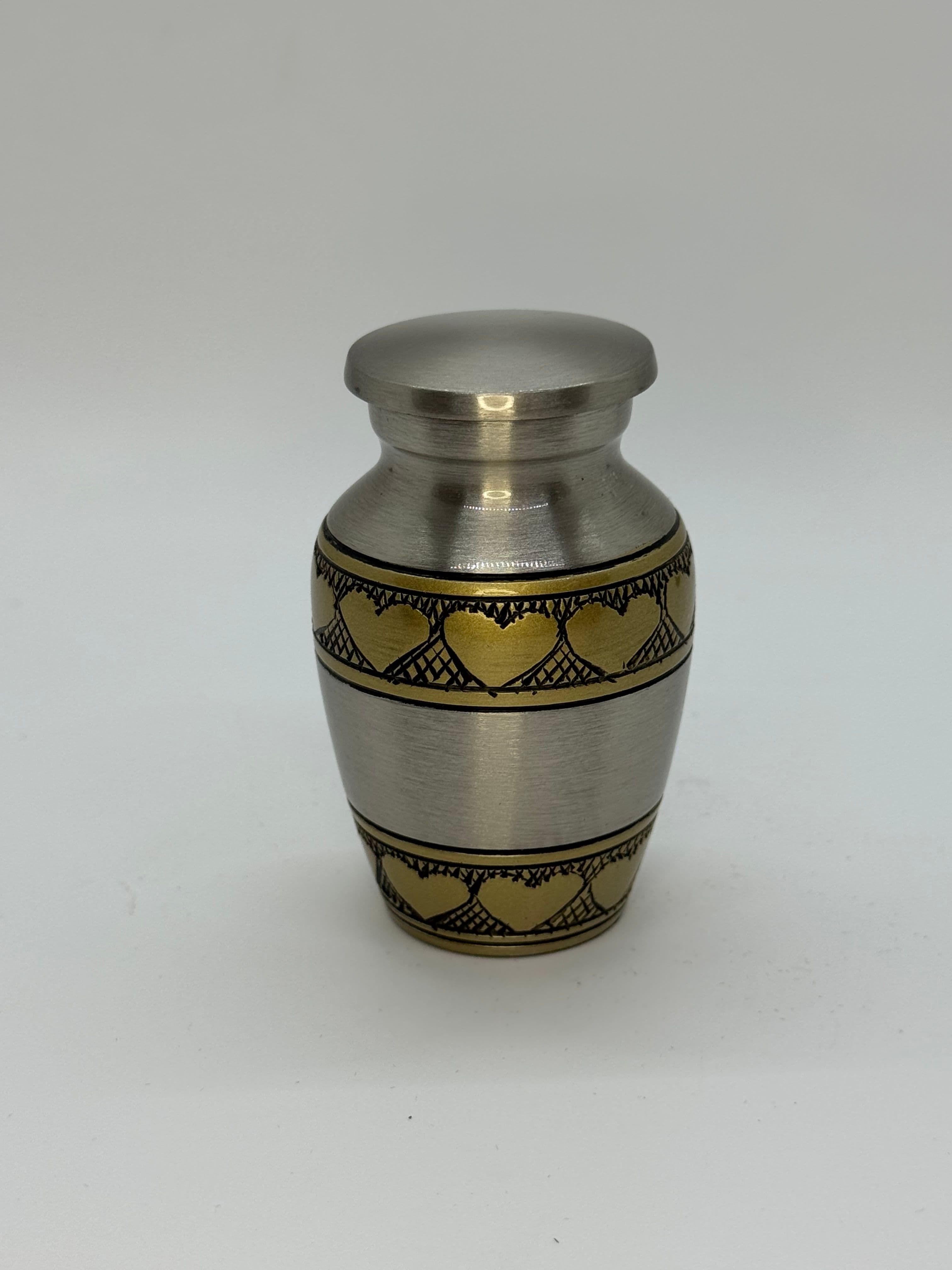 Small metal keepsake urn featuring brass heart etchings.